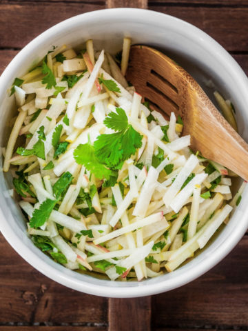 jicama apple salad in white bowl with wooden spoon