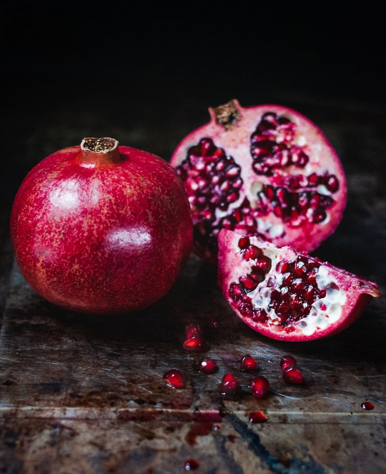 pomegranate whole with another cut open exposing seeds