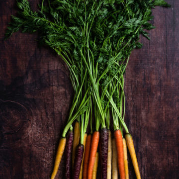rainbow carrots with carrot tops on dark background overhead