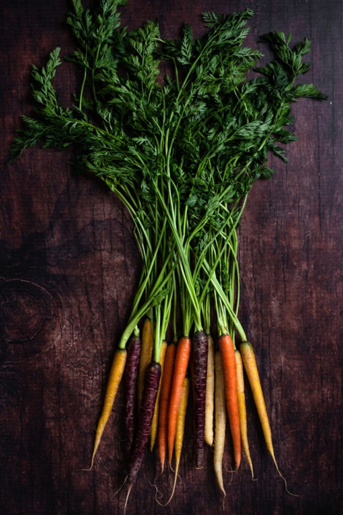 rainbow carrots with carrot tops on dark background overhead