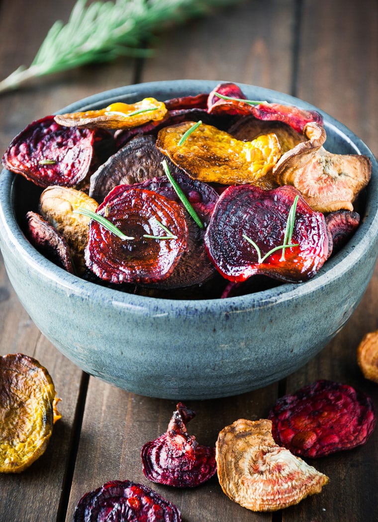 rosemary beet chips in a blue bowl with beet chip scattered in front of bowl