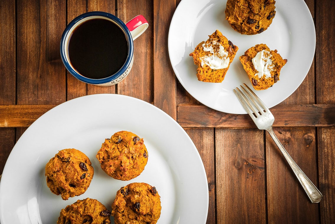 pumpkin raisin muffins on two plates with coffee