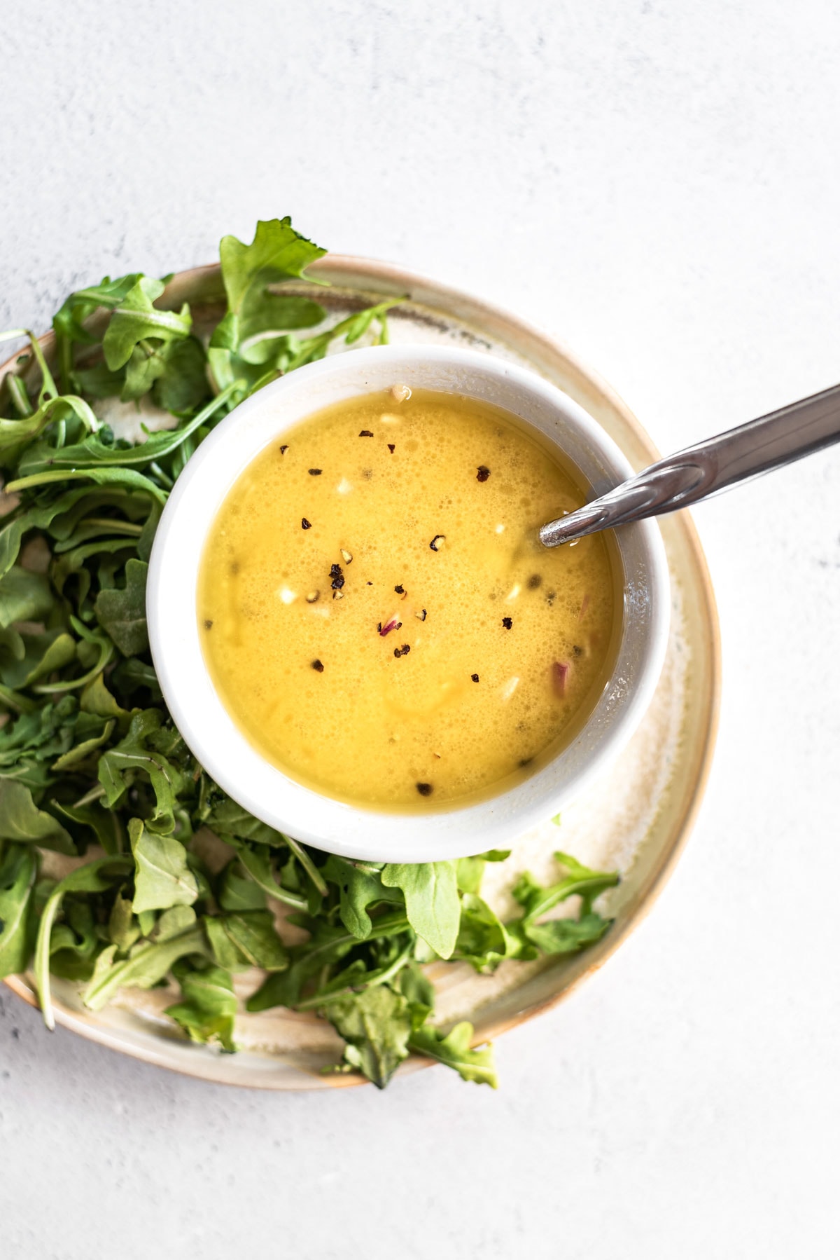 lemon dijon dressing in bowl with spoon and greens on a plate