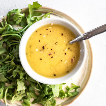 lemon dijon dressing in bowl with spoon on a plate with greens