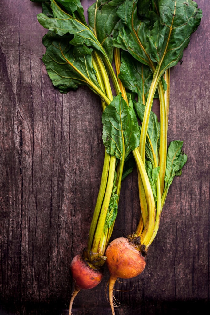 two beets with stems and greens on wood background