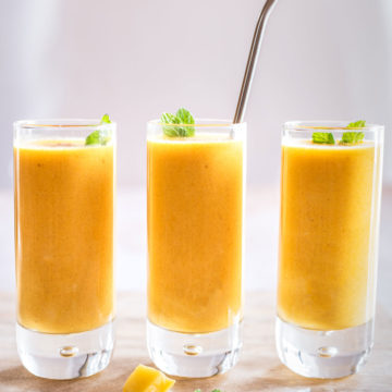 mango rum lassi in three glasses straight on with straw in middle glass