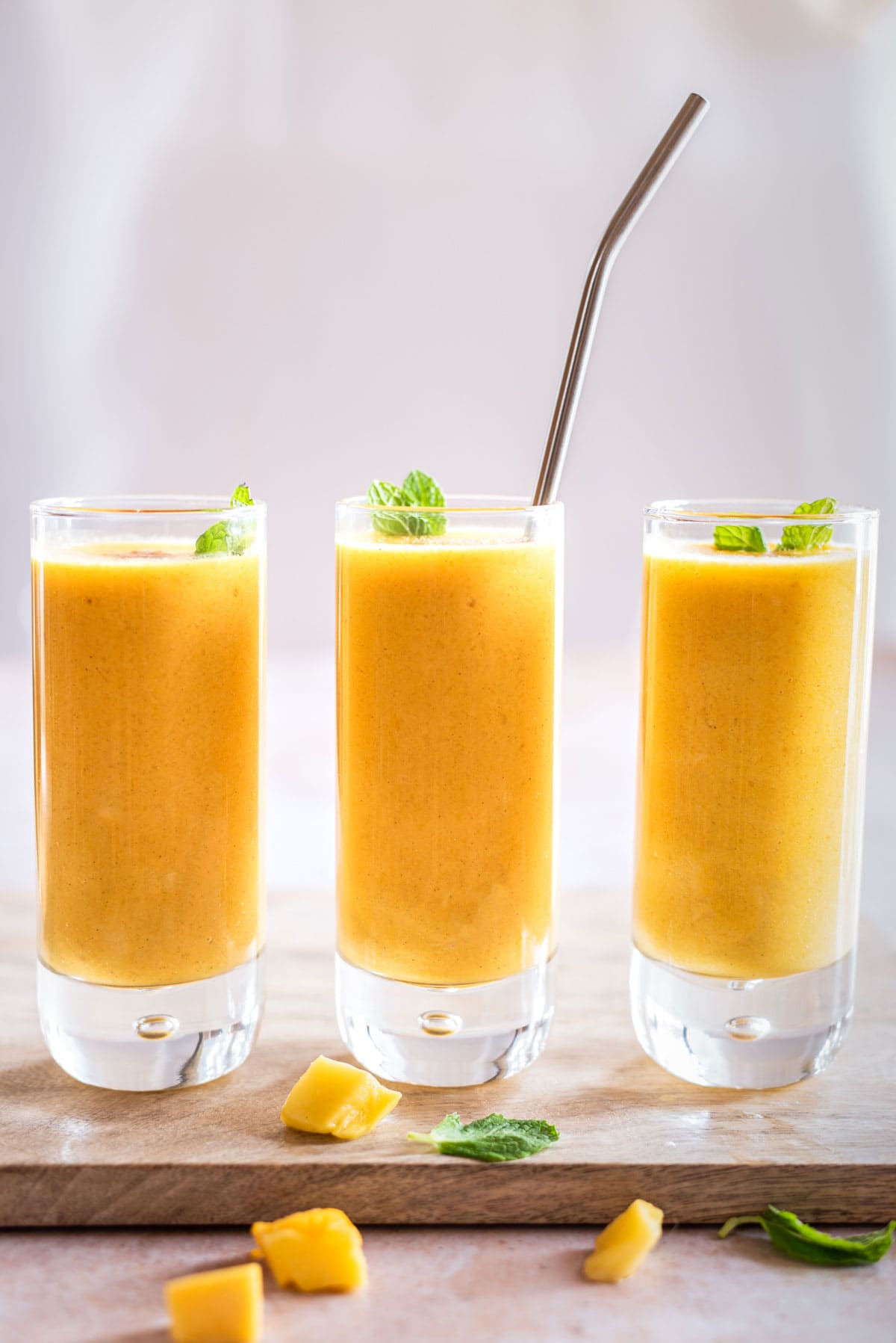 mango rum lassi in three glasses straight on with straw in middle glass