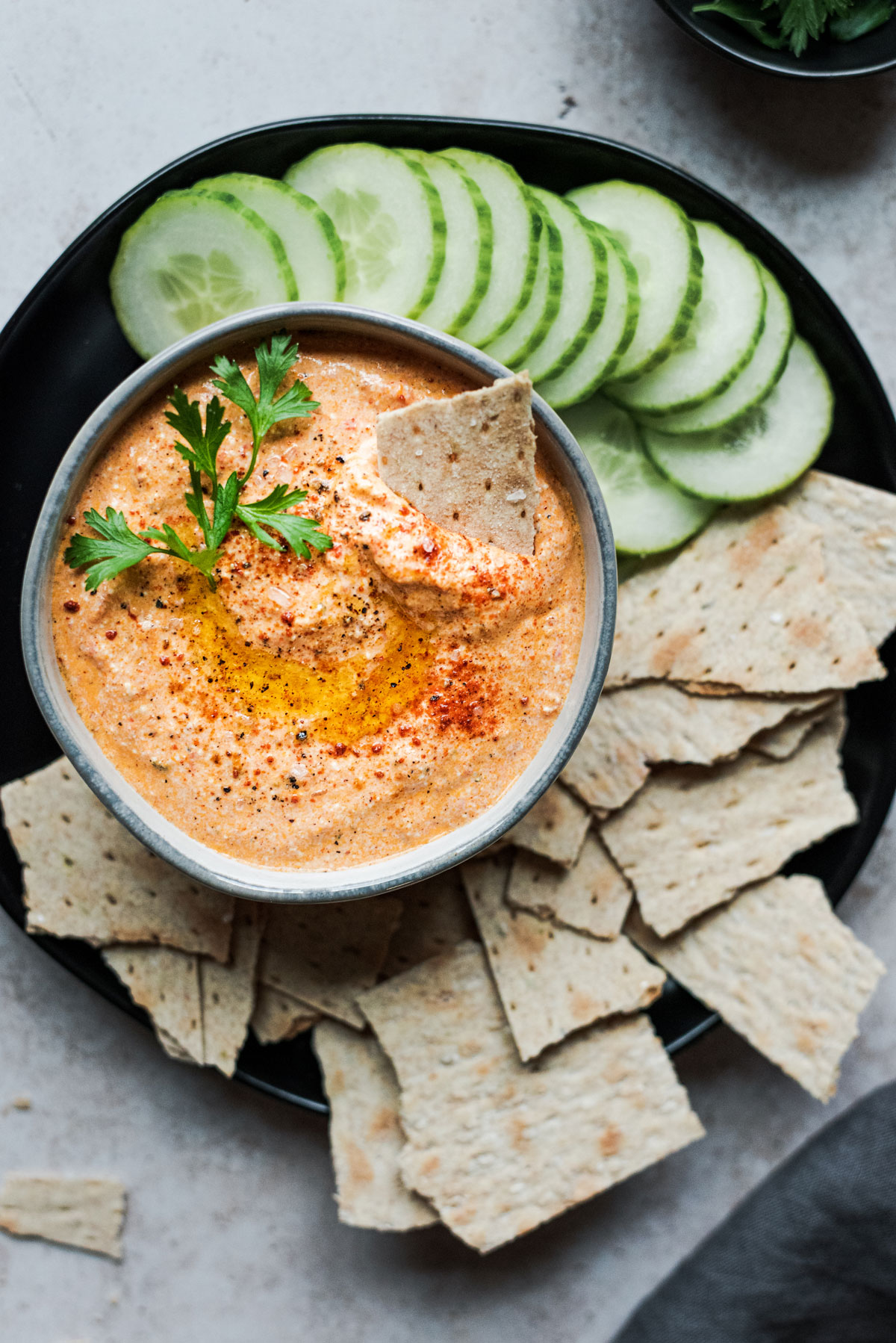 red pepper feta dip with crackers and cucumber overhead on black plate