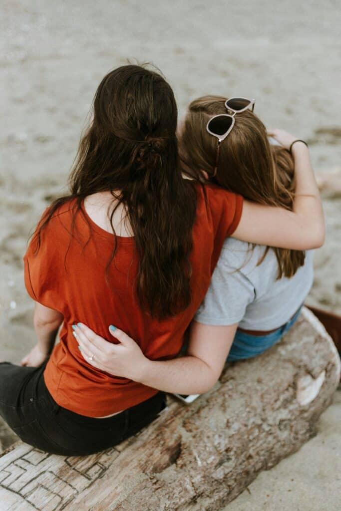 Two girls with their backs to the camera, sitting side by side with their arms around each other