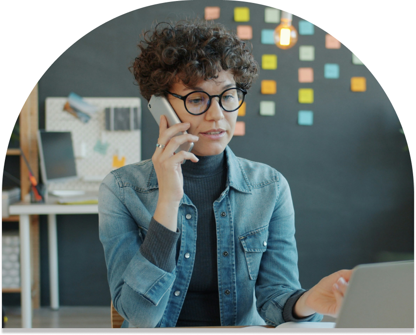 woman talking on phone. she is wearing a denim jacket and is wearing glasses