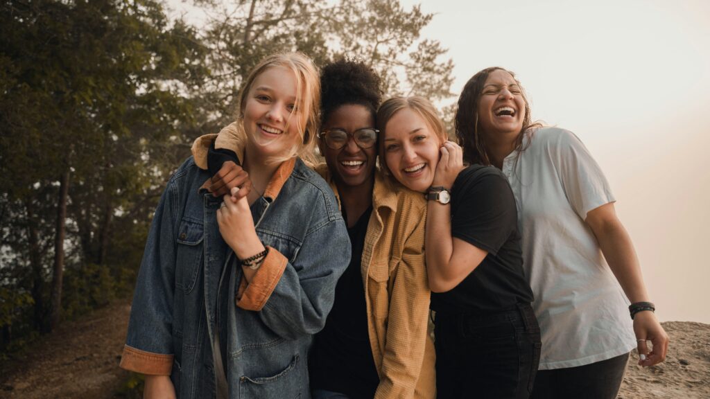four women standing together smiling at the camera. They are outside