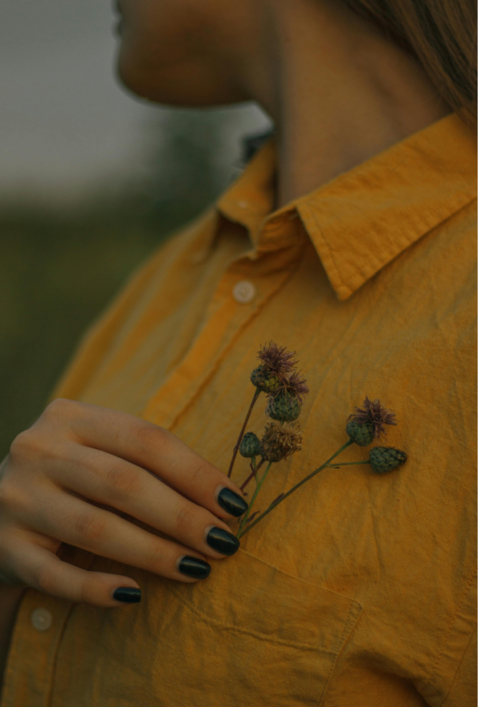 woman wearing a yellow shirt holding flowers at her chest. She is looking away from the camera